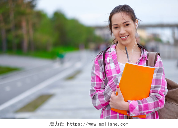 微笑的亚洲女学生微笑的亚洲女学生与文件夹和背包在绿色的夏季公园。教育、校园和青少年观念